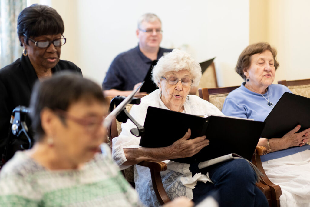 Grace_Management_Memphis_2018-1932-2 - Collier Park A group of seniors are sitting in a music class, holding folders with sheet music and singing together at Collier Park, offering senior living near Lake Charles, LA.
