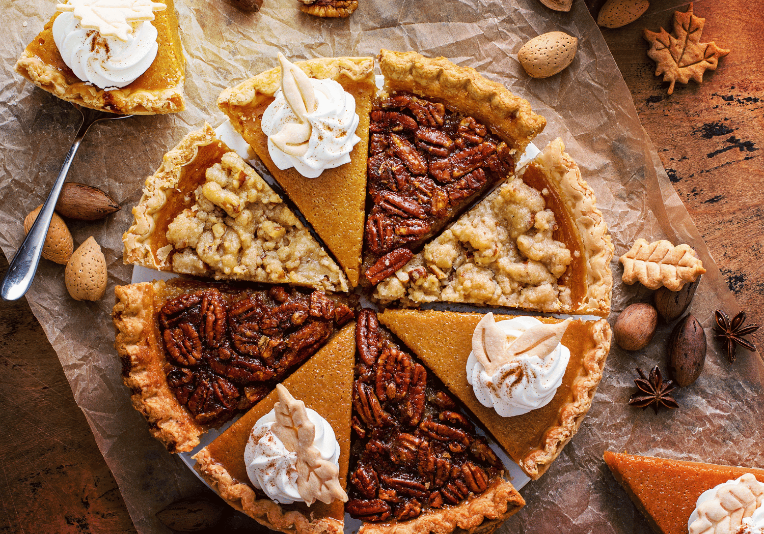 Assorted autumn-tinted mini pies arranged in a circular pie, each with whipped cream toppings and pecans on parchment paper.